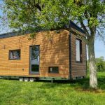 kleines haus auf rädern von team tiny house mit holzfassade auf grüner wiese mit holzfenstern